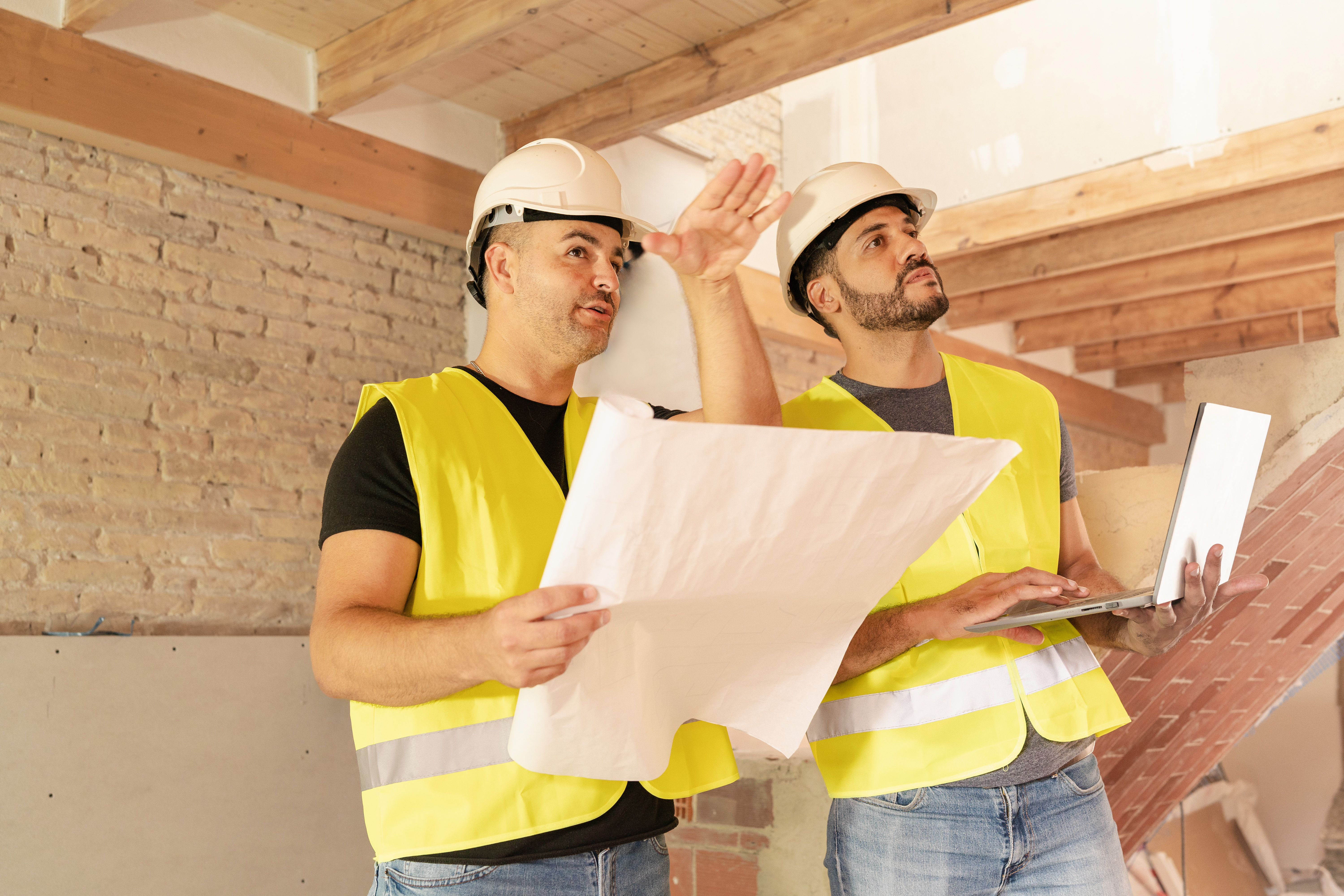 Two construction workers wearing safety vests and hardhat working with laptop on a construction site